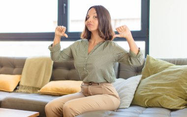 Genç Latin bir kadın gururlu, kibirli ve kendinden emin, tatmin olmuş ve başarılı görünüyor, kendini işaret ediyor. ev kavramı