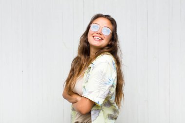 Genç ve güzel bir kadın neşeyle gülümsüyor, mutlu, tatmin olmuş ve rahatlamış hissediyor, kollarını kavuşturup yan tarafa bakıyor. turizm konsepti