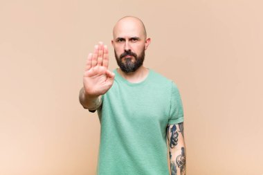 Genç, kel ve sakallı bir adam ciddi, sert, hoşnutsuz ve kızgın görünüyor.