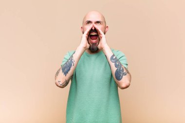 Genç kel ve sakallı bir adam mutlu, heyecanlı ve pozitif hissediyor. Elleri ağızının yanında bağırıyor, bağırıyor.