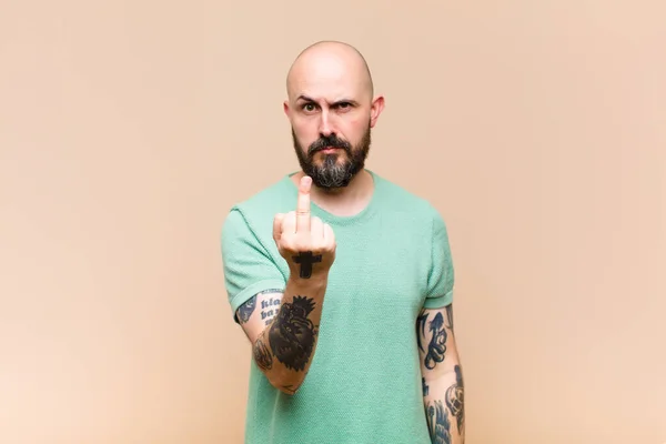 young bald and bearded man feeling angry, annoyed, rebellious and aggressive, flipping the middle finger, fighting back