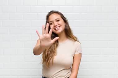 Gülümsüyor ve dost canlısı görünüyor, 5 ya da 5 numarayı gösteriyor, el önde, geriye doğru sayıyor.