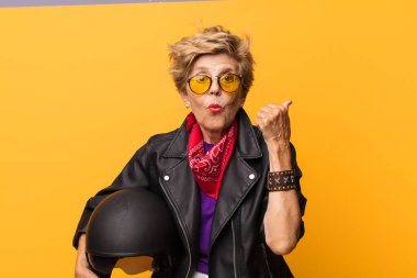 Olgun, yaşlı, güzel bir kadın inançsızlıktan şaşkın şaşkın bakıyor, yan taraftaki objeyi işaret ediyor ve 