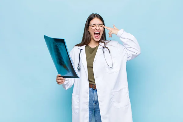 young pretty physician looking unhappy and stressed, suicide gesture making gun sign with hand, pointing to head