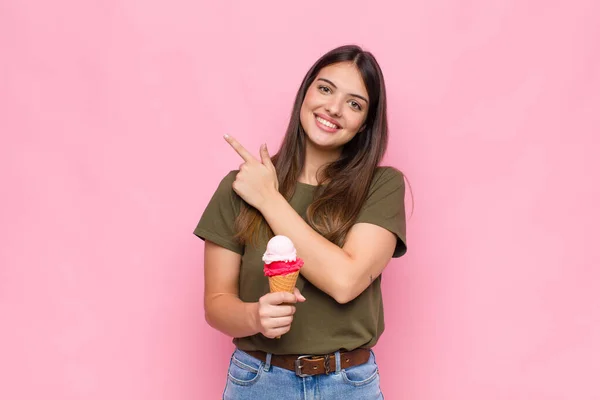 アイスクリームを手にした若い可愛い女性は陽気に笑顔を浮かべ幸せを感じ横と上を指差してコピースペースに物体を見せ — ストック写真