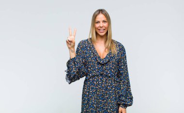 Genç, güzel bir kadın gülümsüyor ve arkadaş canlısı görünüyor. İki ya da iki numarayı gösteriyor. Elleri önde, geri sayıyor.