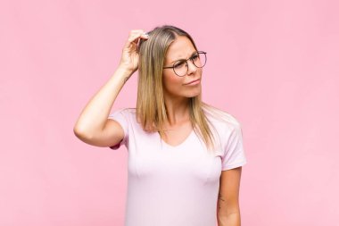 Genç, güzel bir kadın şaşkın ve kafası karışmış hissediyor, başını kaşıyor ve yan tarafa bakıyor.