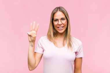 Genç, güzel bir kadın gülümsüyor ve arkadaş canlısı görünüyor. Üç ya da üç numarayı gösteriyor. Elleri önde, geriye doğru sayıyor.