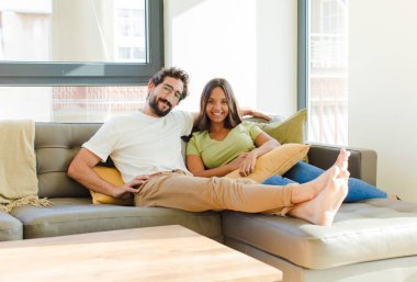 Genç çift mutlu bir şekilde gülümsüyor, elleri kalçalarında ve kendinden emin, olumlu, gururlu ve arkadaş canlısı bir tavırla. yeni ev kavramı