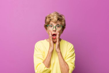 Yaşlı güzel kadın şok olmuş ve korkmuş hissediyor, ağzı açık ve elleri yanaklarında korkmuş görünüyor.