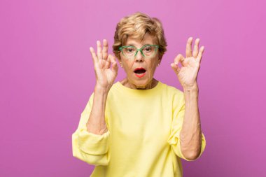 Yaşlı güzel kadın şok olmuş, şaşırmış ve şaşırmış hissediyor. İki eliyle de onay işareti yapıyor.