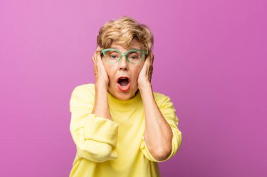 Yaşlı, hoş olmayan, şaşkın, korkmuş ya da endişeli görünen, ağzı açık ve iki kulağını da elleriyle kapatan güzel bir kadın.