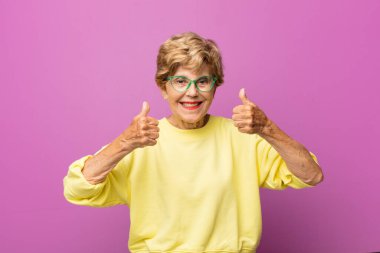 old pretty woman smiling broadly looking happy, positive, confident and successful, with both thumbs up clipart