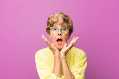 Yaşlı güzel bir kadın beklenmedik bir sürprizden dolayı şaşkın ve heyecanlı, güler yüzlü ve mutlu hissediyor.