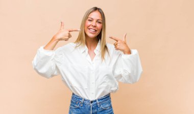 Genç, güzel bir kadın, kendine güvenerek gülümsüyor. Kendi gülüşünü gösteriyor. Olumlu, rahat, tatmin olmuş bir tavır.
