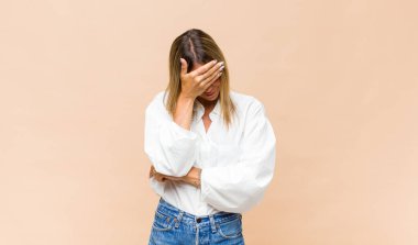 Genç, güzel bir kadın stresli, utanmış ya da üzgün görünüyor. Baş ağrısı var, yüzü elle kapatılmış.