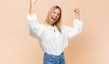 Genç ve güzel bir kadın muzaffer bir şekilde bağırıyor. Heyecanlı, mutlu ve şaşırmış görünüyor. Kutlama yapıyor.