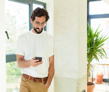 Evde sakallı genç bir adam var. Akıllı telefon kullanarak.