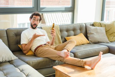 Genç sakallı havalı adam evdeki kanepede oturuyor.