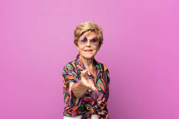 старая симпатичная женщина улыбается, выглядит счастливой, уверенной и дружелюбной, предлагает рукопожатие для заключения сделки, содействует