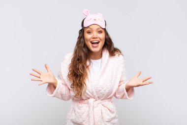young pretty woman feeling happy, excited, surprised or shocked, smiling and astonished at something unbelievable wearing pajama