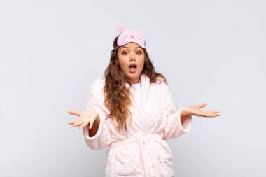 young pretty woman open-mouthed and amazed, shocked and astonished with an unbelievable surprise wearing pajama