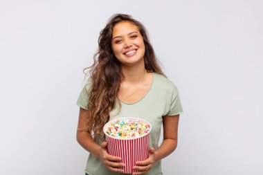 young woman with a pop conrs bucket smiling happily with a hand on hip and confident, positive, proud and friendly attitude