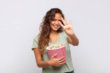 young woman with a pop conrs bucket smiling and looking friendly, showing number four or fourth with hand forward, counting down