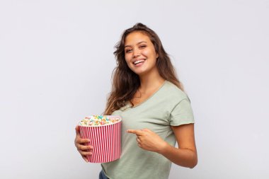 young woman with a pop conrs bucket looking excited and surprised pointing to the side and upwards to copy space