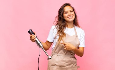 Genç kadın fırıncı neşeli bir şekilde gülümsüyor, mutlu hissediyor ve kenarı ve yukarıyı işaret ediyor, fotokopi uzayındaki nesneleri gösteriyor