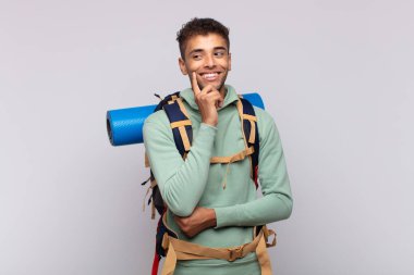 young hiker man smiling happily and daydreaming or doubting, looking to the side