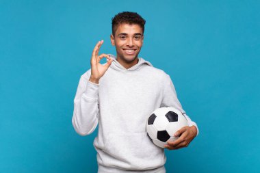 young man feeling happy, relaxed and satisfied, showing approval with okay gesture, smiling. soccer concept
