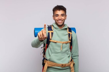 young hiker man smiling and looking friendly, showing number one or first with hand forward, counting down