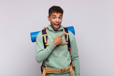 young hiker man looking excited and surprised pointing to the side and upwards to copy space