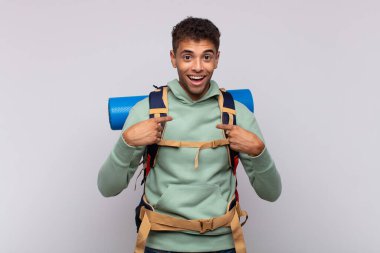 young hiker man feeling happy, surprised and proud, pointing to self with an excited, amazed look
