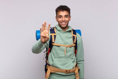 young hiker man smiling and looking friendly, showing number four or fourth with hand forward, counting down