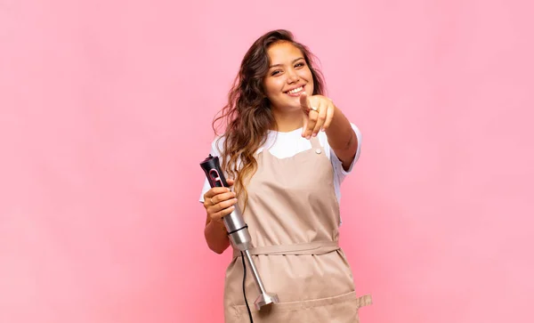 young woman baker pointing at camera with a satisfied, confident, friendly smile, choosing you