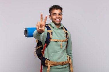 young hiker man smiling and looking happy, carefree and positive, gesturing victory or peace with one hand