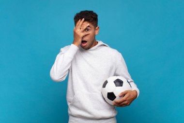 young man looking shocked, scared or terrified, covering face with hand and peeking between fingers. soccer concept