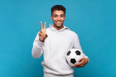 young man smiling and looking friendly, showing number two or second with hand forward, counting down. soccer concept