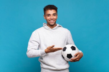 young man smiling cheerfully, feeling happy and showing a concept in copy space with palm of hand. soccer concept