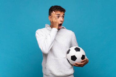 young man feeling happy, excited and surprised, looking to the side with both hands on face. soccer concept