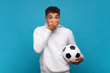 young man covering mouth with hands with a shocked, surprised expression, keeping a secret or saying oops. soccer concept