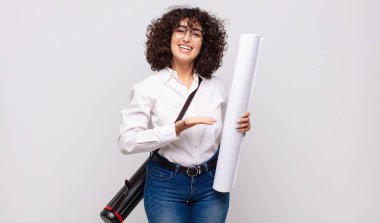 Genç mimar kadın neşeli bir şekilde gülümsüyor, mutlu hissediyor ve fotokopi alanında bir konsept gösteriyor.