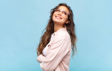 Kız neşeyle gülümsüyor, mutlu, tatmin olmuş ve rahatlamış hissediyor, kollarını kavuşturup yan tarafa bakıyor.