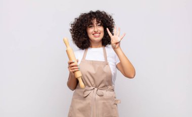 Genç ve güzel bir kadın şef gülümsüyor ve arkadaş canlısı görünüyor, 4 ya da 4 numarayı gösteriyor, elleri önde, geriye doğru sayıyor.
