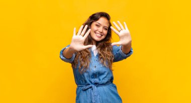 Kız gülümsüyor ve arkadaş canlısı görünüyor, onuncu ya da onuncu numarayı gösteriyor, eli önde, geri sayıyor.