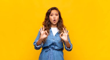 Şok olmuş, şaşırmış ve şaşırmış hisseden bir kız, iki eliyle onay işareti yapıyor.