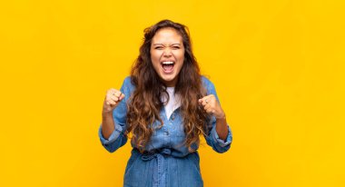 Kızgın bir ifadeyle ya da yumruklarıyla başarıyı kutlayan bir şekilde bağıran bir kız.