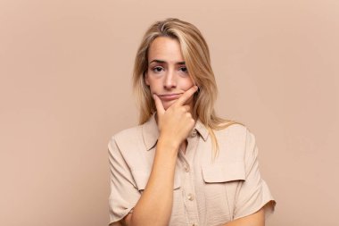 Ciddi, düşünceli ve güvensiz görünen bir kadın. Bir kolu çapraz ve eli çenesinde, seçenekleri değerlendiriyor.